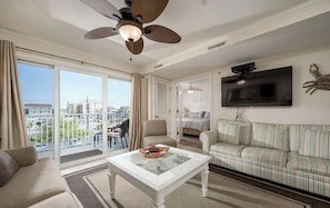Un salon spacieux doté d’une grande fenêtre, d’un ventilateur de plafond, d’un téléviseur à écran plat et d’un canapé à rayures.
