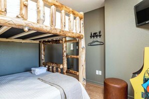 A bunk bed with a wooden ladder, a small stool, and a TV mounted on the wall.