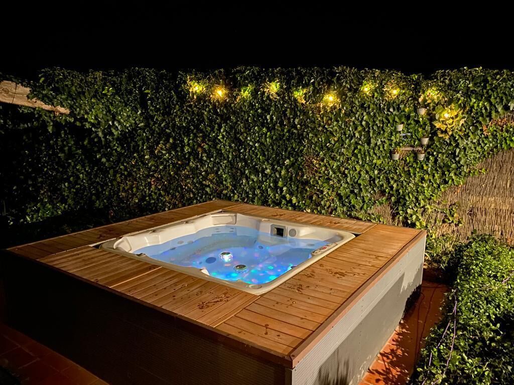 Un jacuzzi con un muelle de madera, rodeado por un seto verde exuberante.