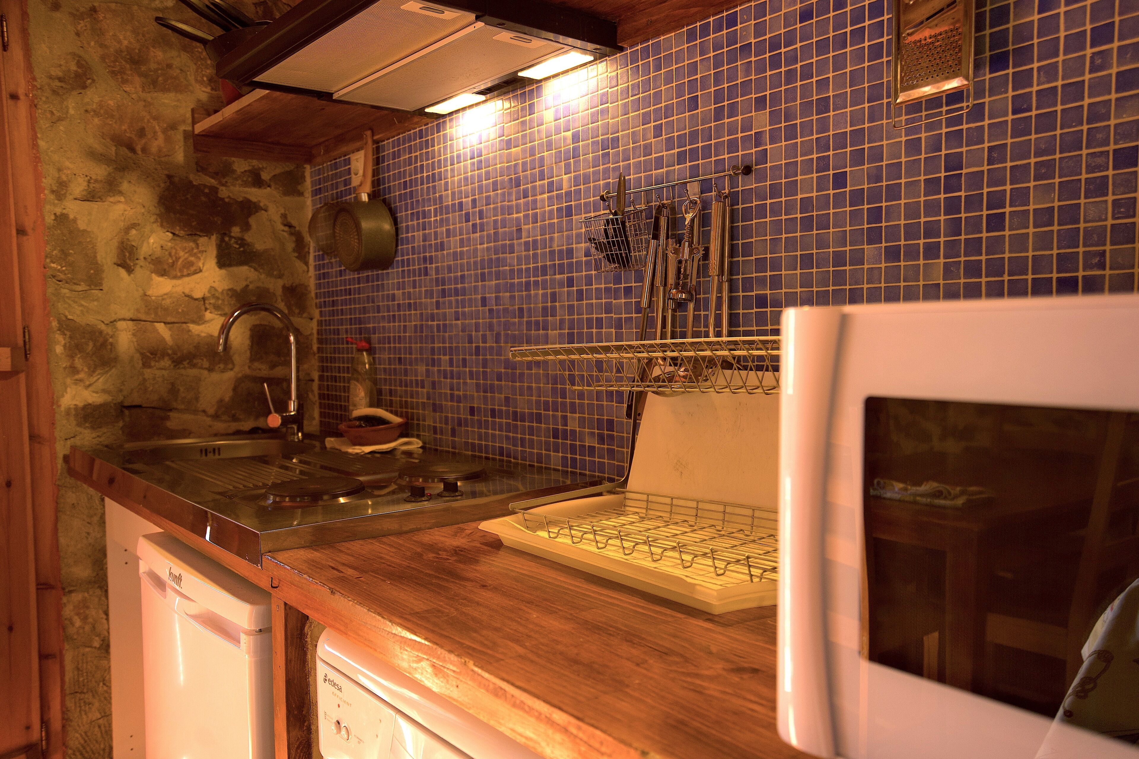 A kitchen with a stone wall, blue tiled backsplash, wooden countertop, and stainless steel appliances.