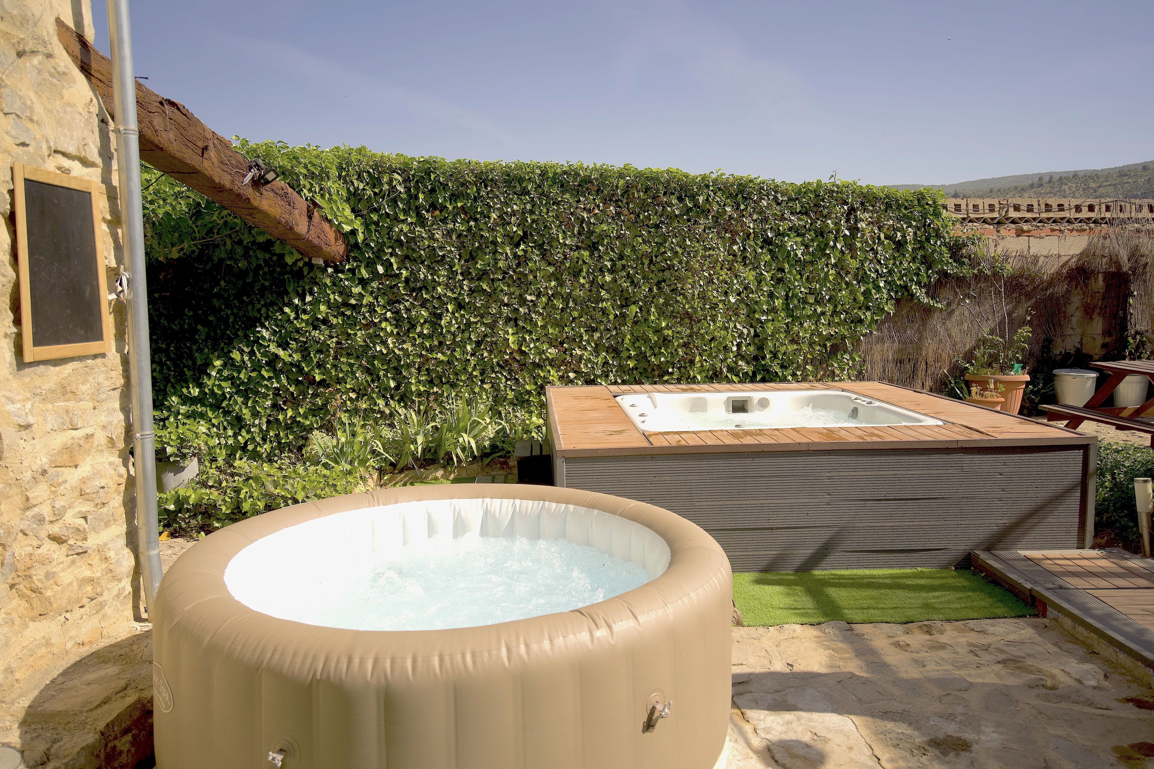 Un jacuzzi y una terraza de madera en un jardín con un muro de piedra y un seto.