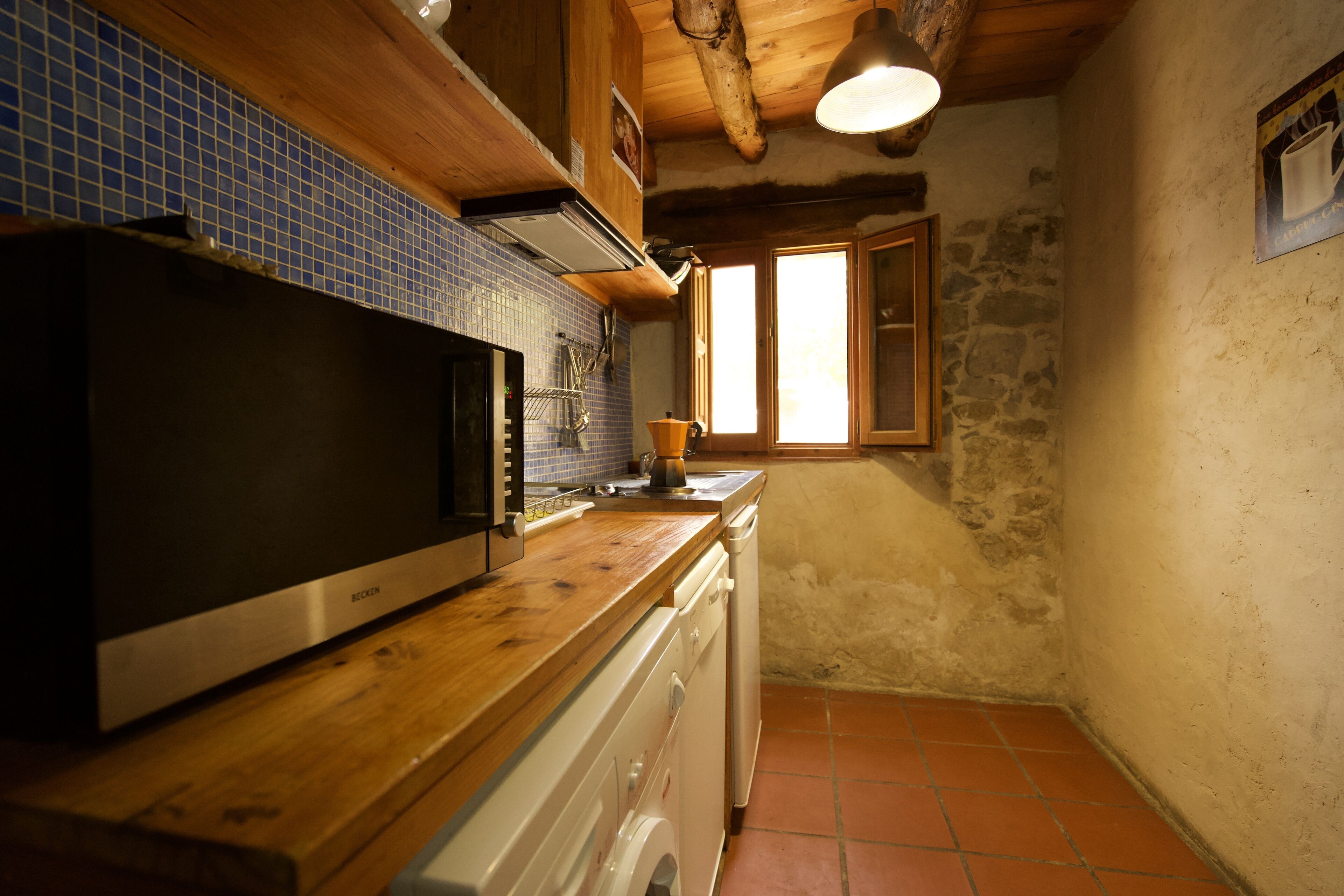 Una cocina con armarios de madera, microondas, pileta y ventana.
