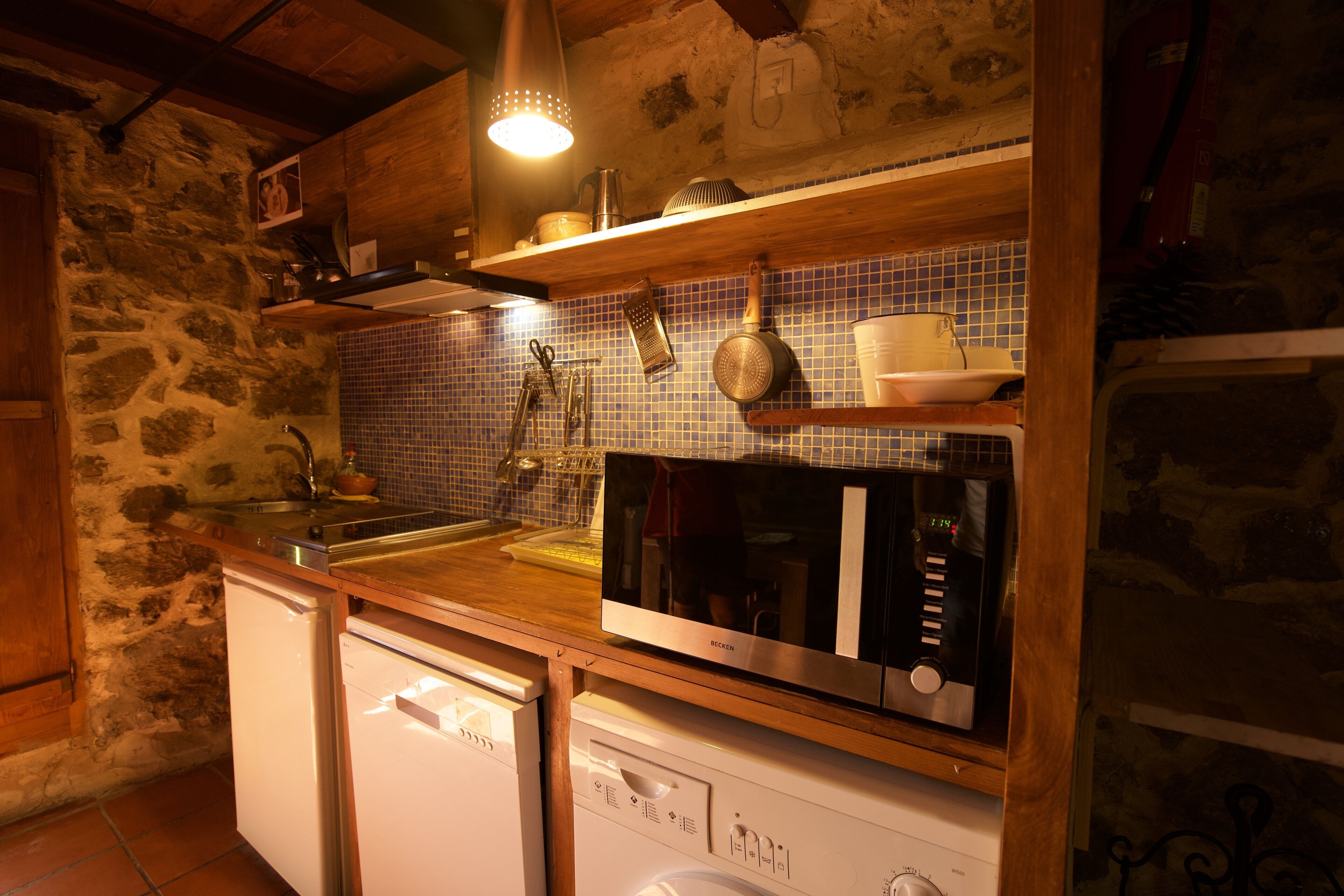 Una cocina con pared de piedra, repisas de madera, microondas y lavavajillas.