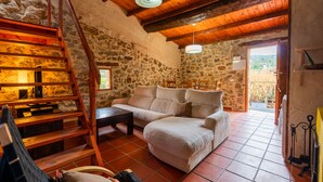 Un intérieur rustique en pierre, avec un escalier en bois, un canapé et une vue sur l’extérieur par une porte ouverte.