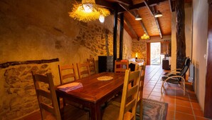 Un coin repas rustique avec une table et des chaises en bois, des murs en pierre et une vue sur un paysage enneigé par une porte ouverte.