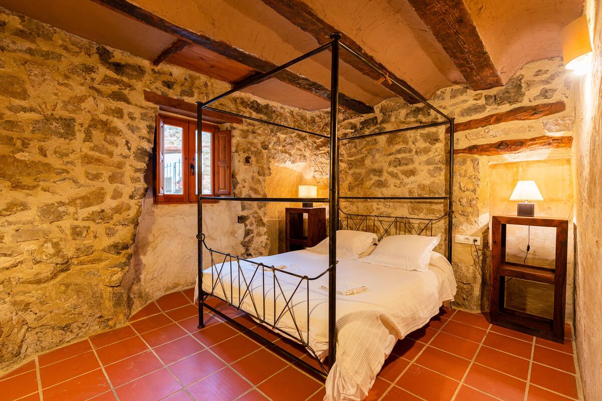 Ein Bett mit Baldachin in einem Zimmer mit Steinwänden, Fliesenboden und Holzbalken.
