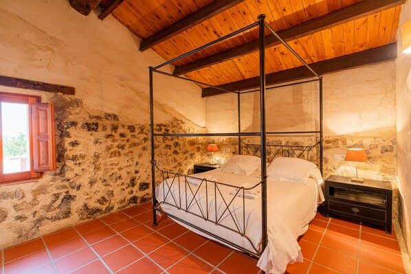 A four-poster bed in a rustic room with stone walls and wooden beams.