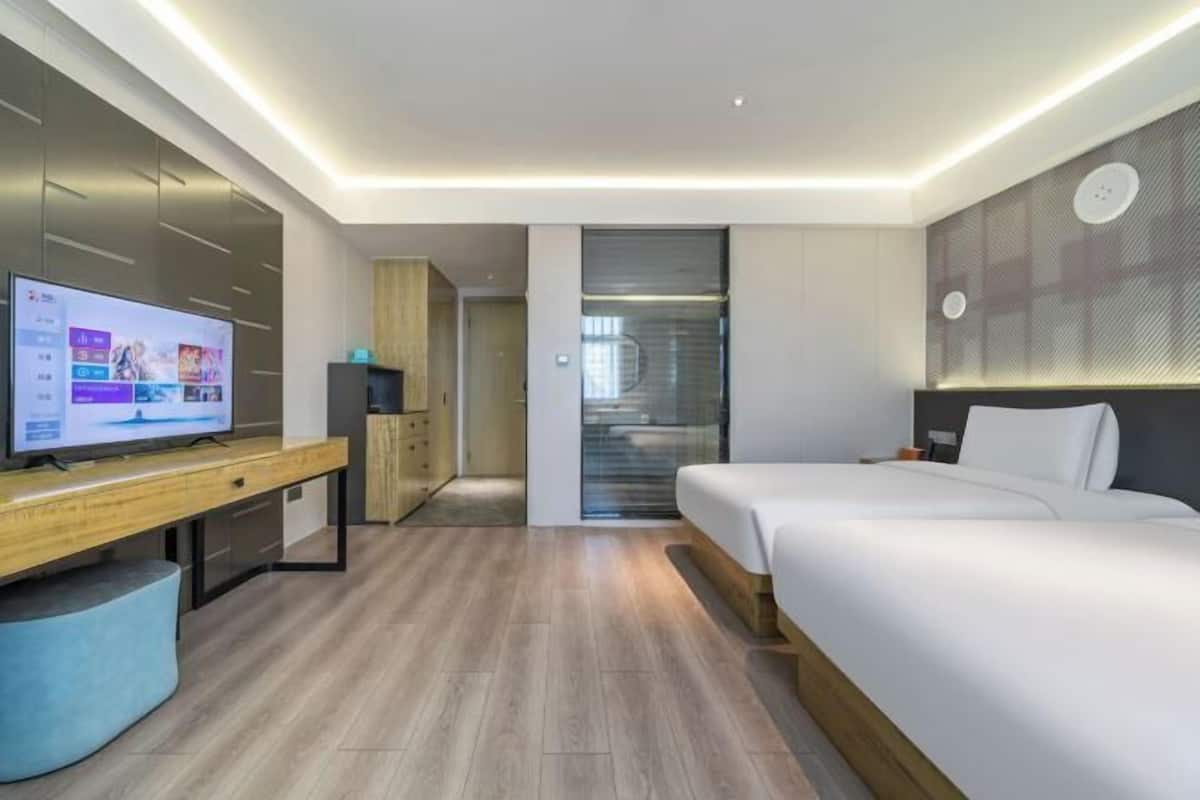 A modern hotel room with a bed, a TV, a desk, and a wardrobe.