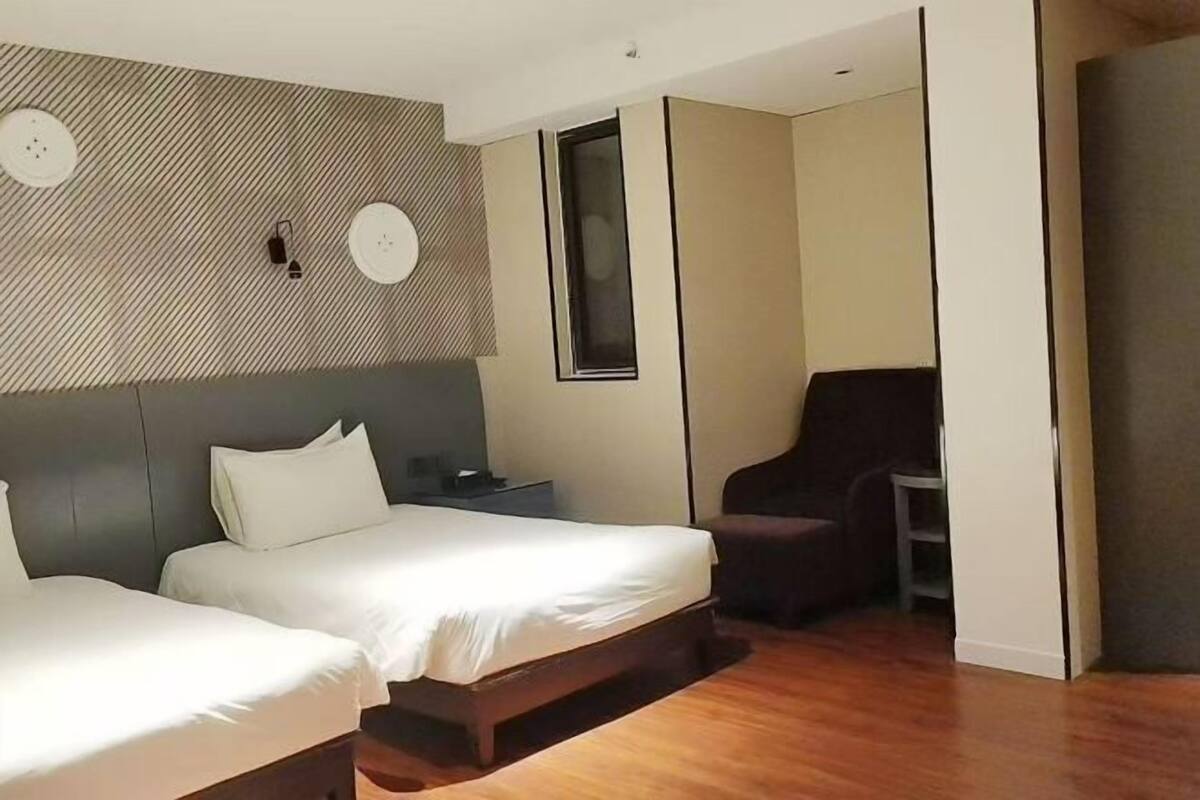 A hotel room with two beds, a small desk, a chair, and a patterned wall.