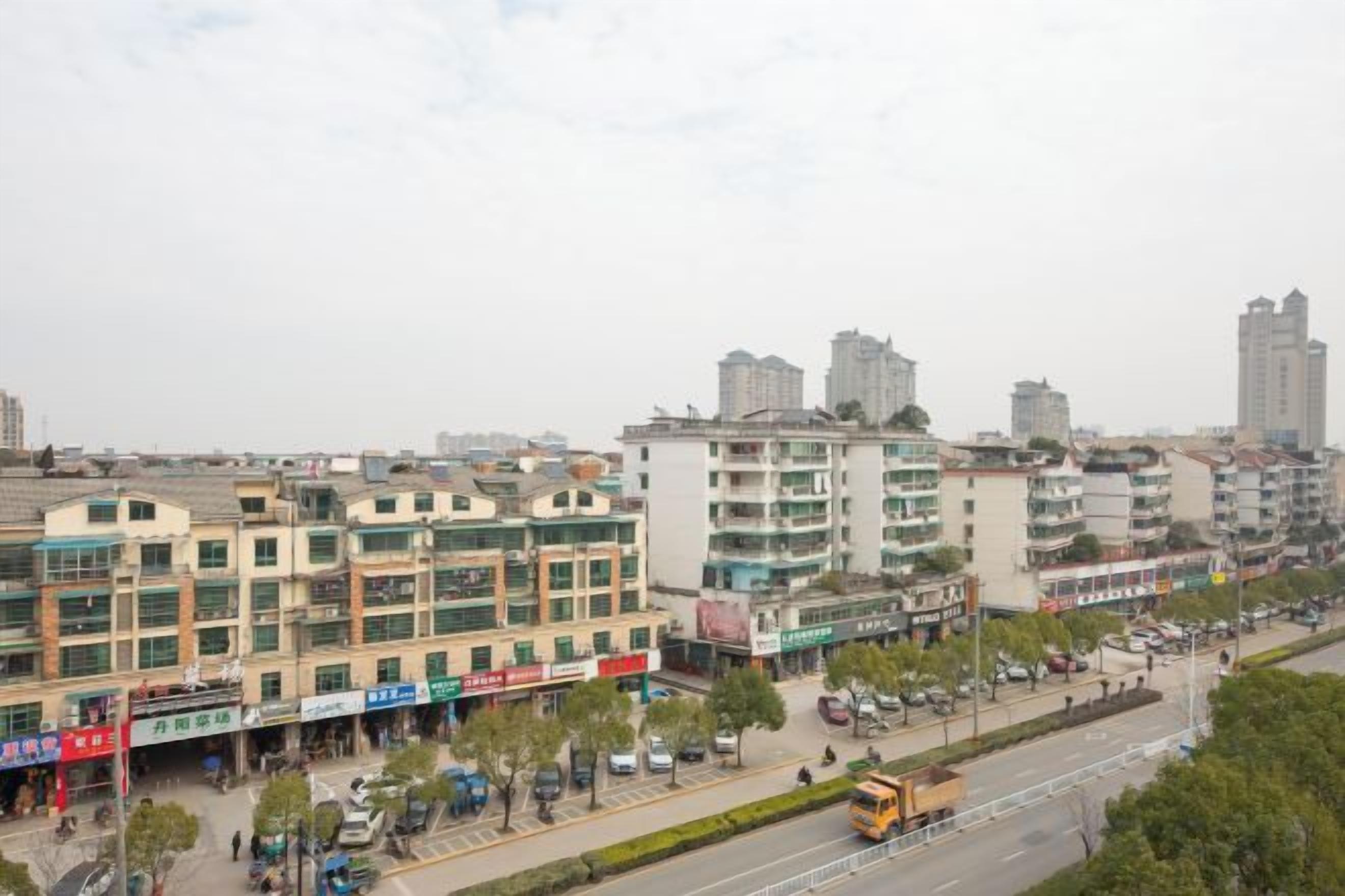A multi-story building with commercial establishments on the ground floor, a clear sky, and a road with vehicles.