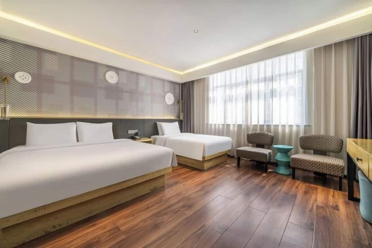 A hotel room with two beds, a desk, a chair, and a large window with curtains.