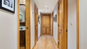 Un pasillo con puertas de madera, una pared blanca y suelo de madera.