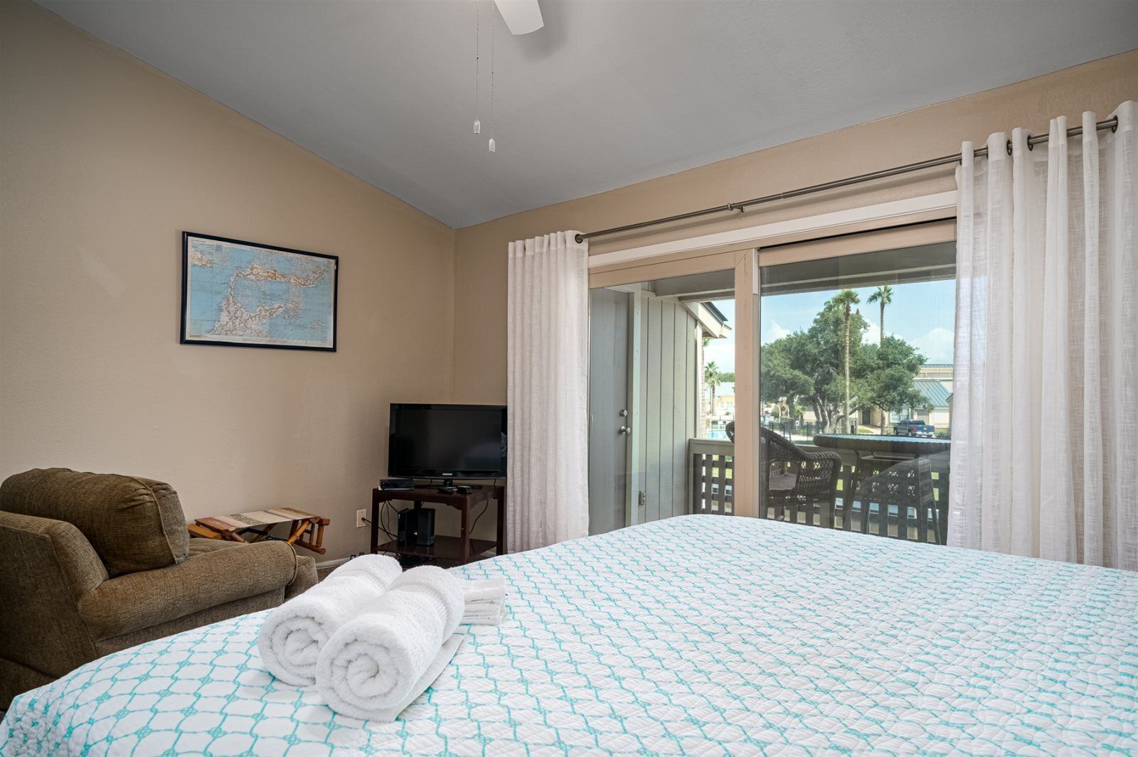 A hotel room with a bed, a television, a couch, and a balcony with a view of palm trees.