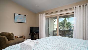 A hotel room with a bed, a television, a couch, and a balcony with a view of palm trees.