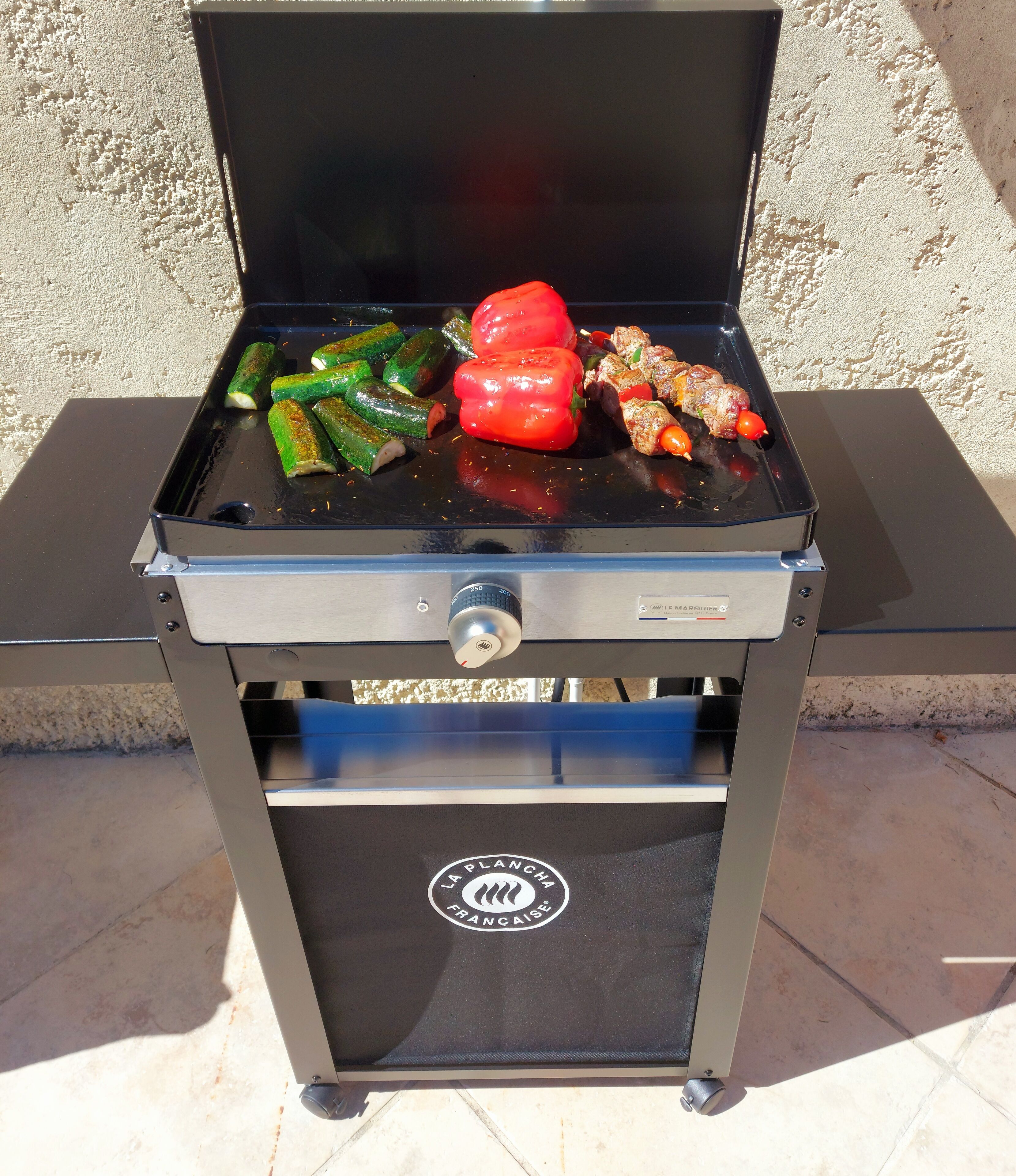 Un barbecue portable doté d’un bouton de contrôle et d’un logo sur le devant, contenant divers légumes et de la viande.