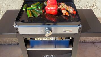 Un barbecue portable doté d’un bouton de contrôle et d’un logo sur le devant, contenant divers légumes et de la viande.