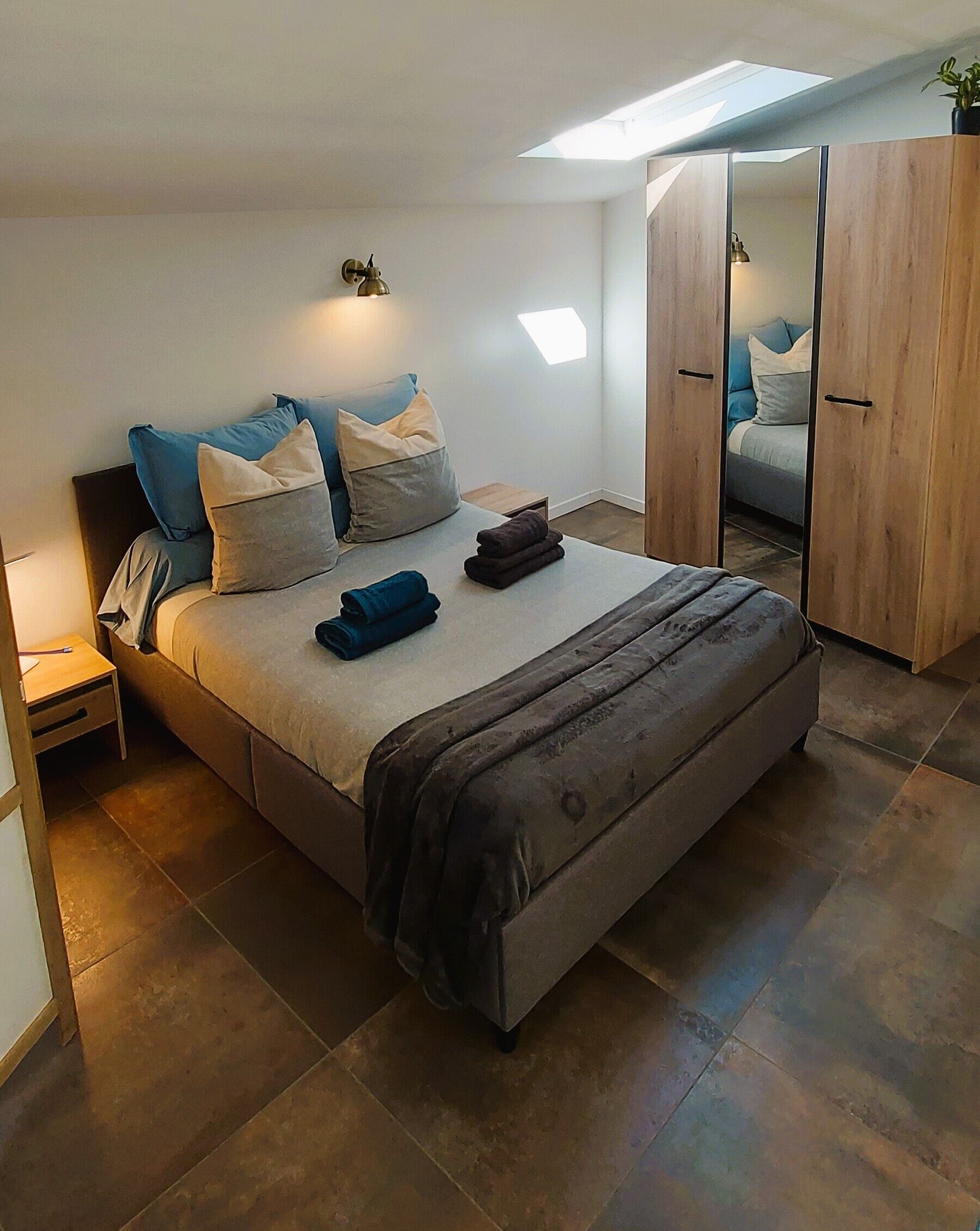 Un dormitorio moderno con una cama grande, una mesita de noche, un armario y un tragaluz.