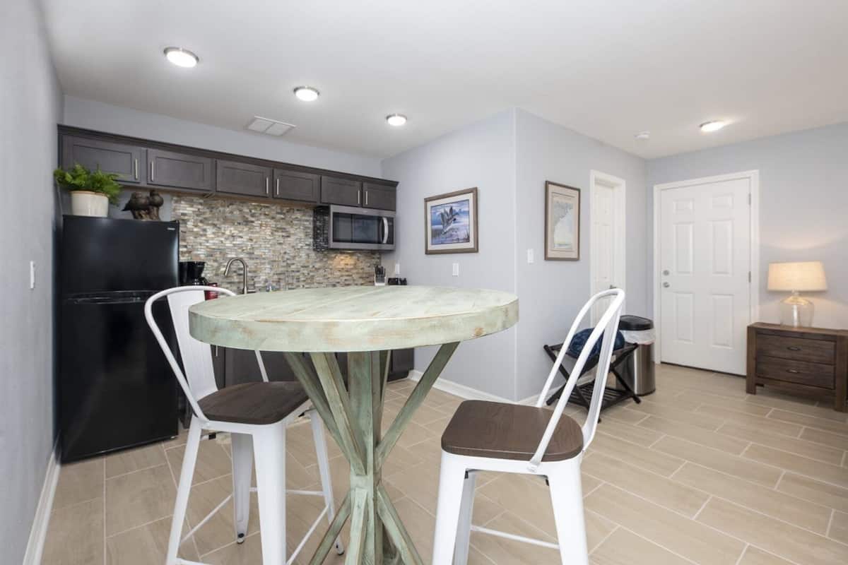 A compact kitchen with a round table, two chairs, a refrigerator, a microwave, and a sink.