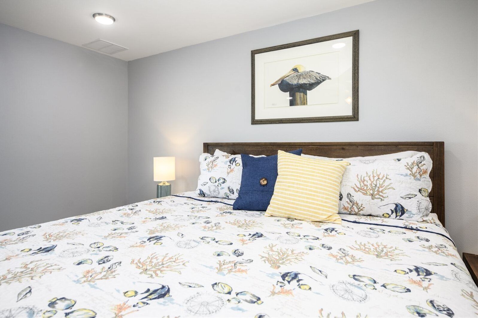 Ein Schlafzimmer mit einem Bett, das eine marine Bettdecke, ein Holz-Kopfteil und ein gerahmtes Bild von einem Pelikan an der Wand hat.
