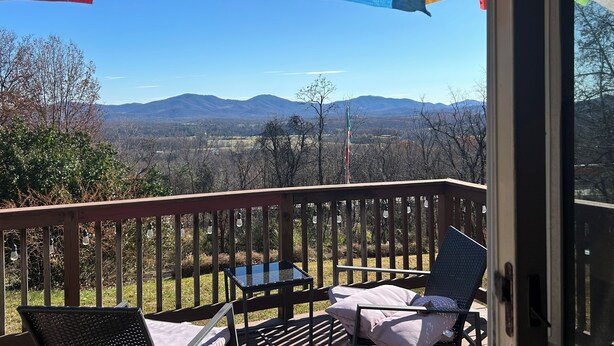 A deck with a view of mountains, a table, and chairs.