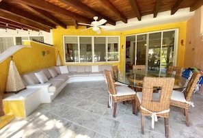 A sunlit patio with a glass table and wicker chairs, a beige sofa, and a ceiling fan. - Amazing Villa in Ixtapa (Troncones)