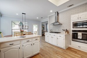 Une cuisine moderne avec des meubles blancs, un îlot central et une hotte de cuisine en acier inoxydable.