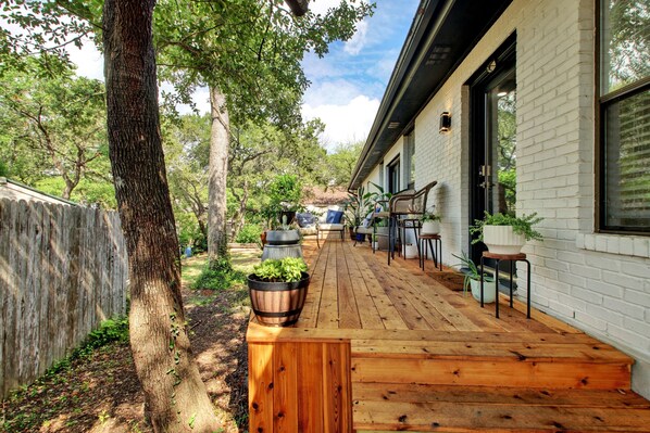 Une terrasse en bois, une maison en briques, du mobilier d’extérieur et des plantes en pot.