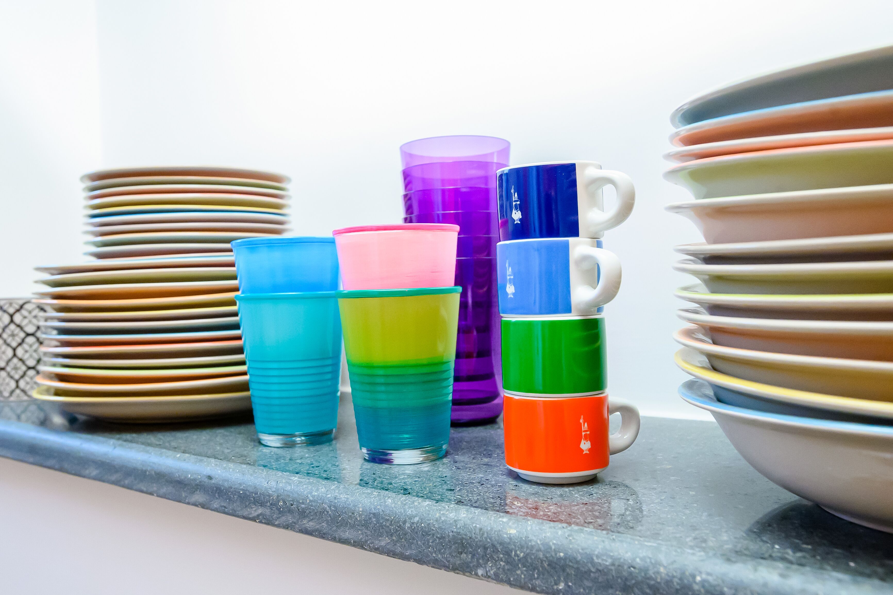 Stacks of colorful plates and cups on a kitchen counter.