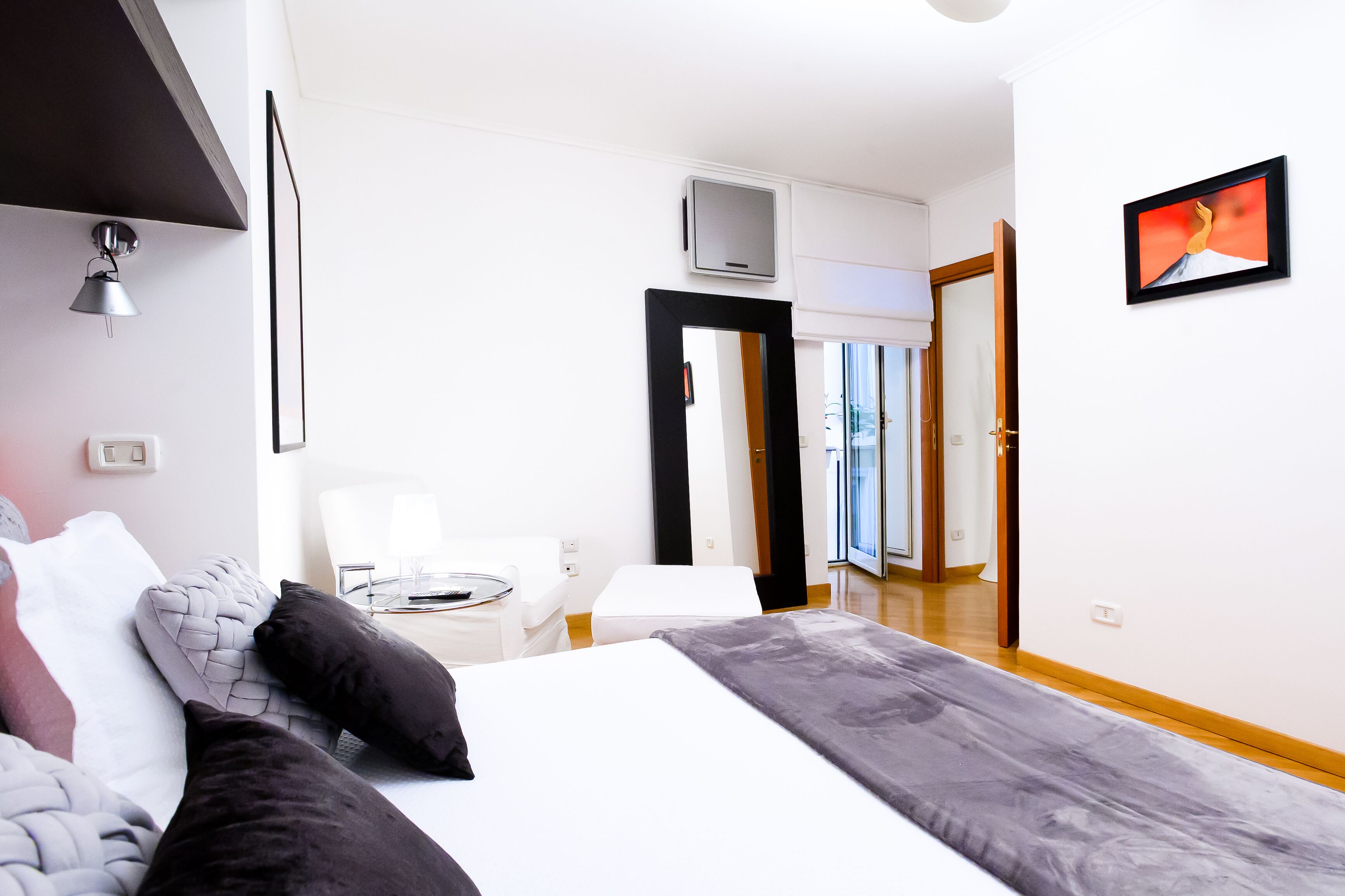 A modern hotel room with a large bed, a desk, and a chair. There is a TV mounted on the wall and a door leading to a balcony.