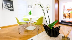 Uma área de refeições moderna com uma mesa redonda branca, cadeiras verdes e um vaso com uma orquídea.