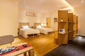 A hotel room with two beds, a desk, a chair, and a small table with items on it.