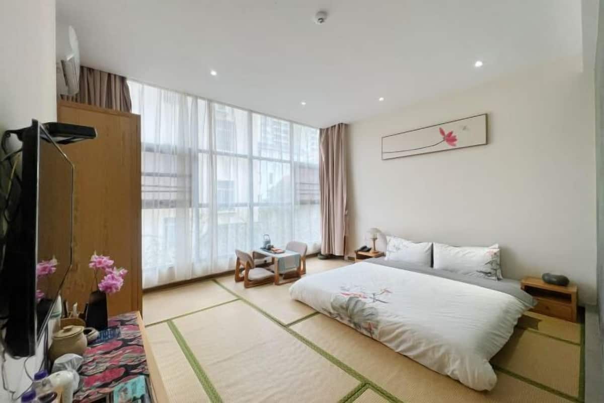 Una habitación de hotel con cama, escritorio, silla, televisión y ventana con cortinas.