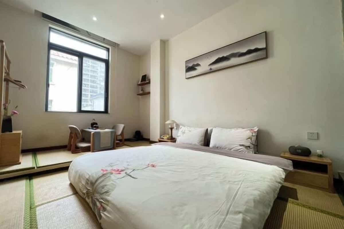 Una habitación de hotel con una cama, una silla, una mesita, una ventana y un cuadro colgado en la pared.