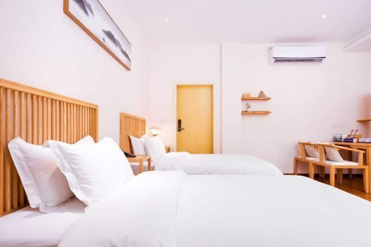 Habitación de hotel con dos camas, cabecero de madera, escritorio con silla, equipo de aire acondicionado y una puerta.