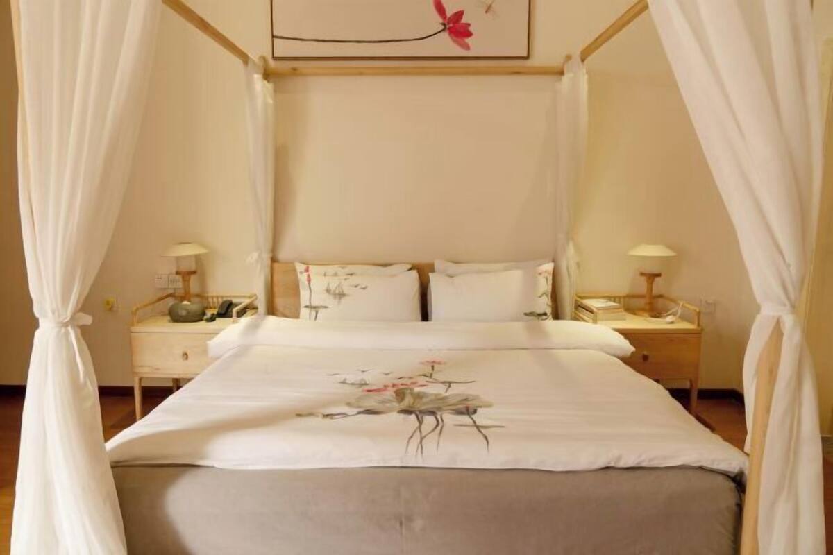Una cama con dosel con un edredón estampado con motivos florales, dos mesitas de noche con lámparas y una obra de arte colgada en la pared.