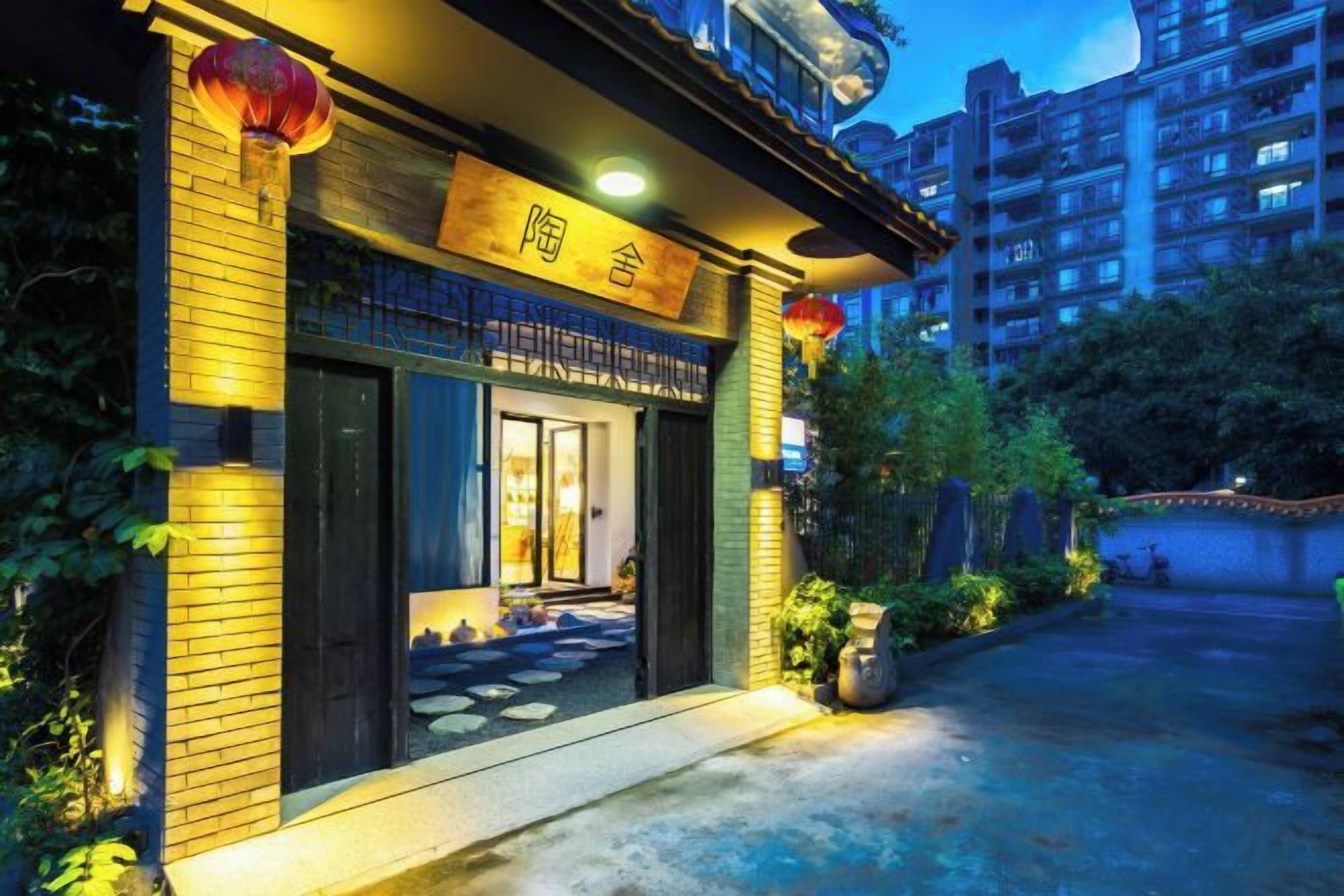 A hotel entrance with a sign, a paved walkway, and a garden area.