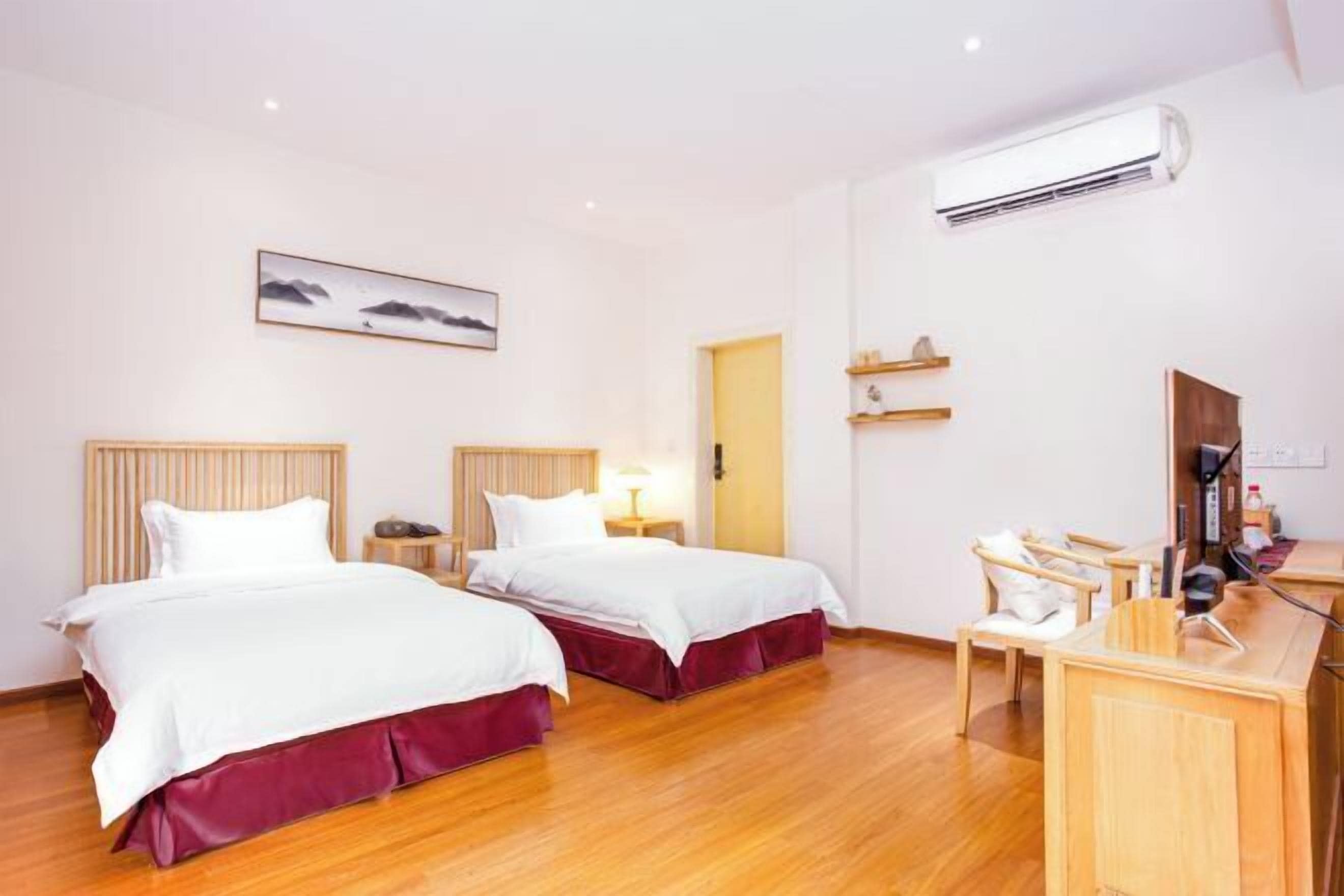 A hotel room with two beds, a desk, a chair, a TV, and an air conditioning unit.
