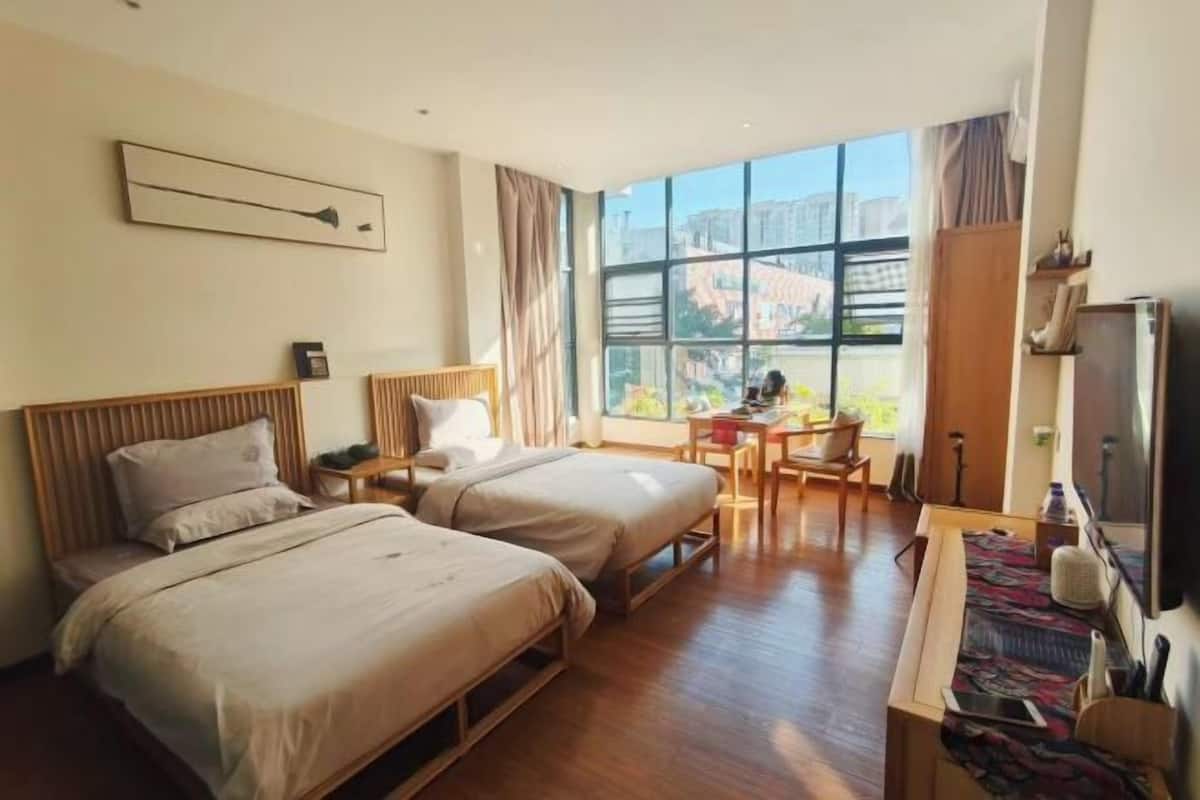 Habitación de hotel con dos camas, un escritorio, una silla, un televisor y un ventanal con vistas a la ciudad.