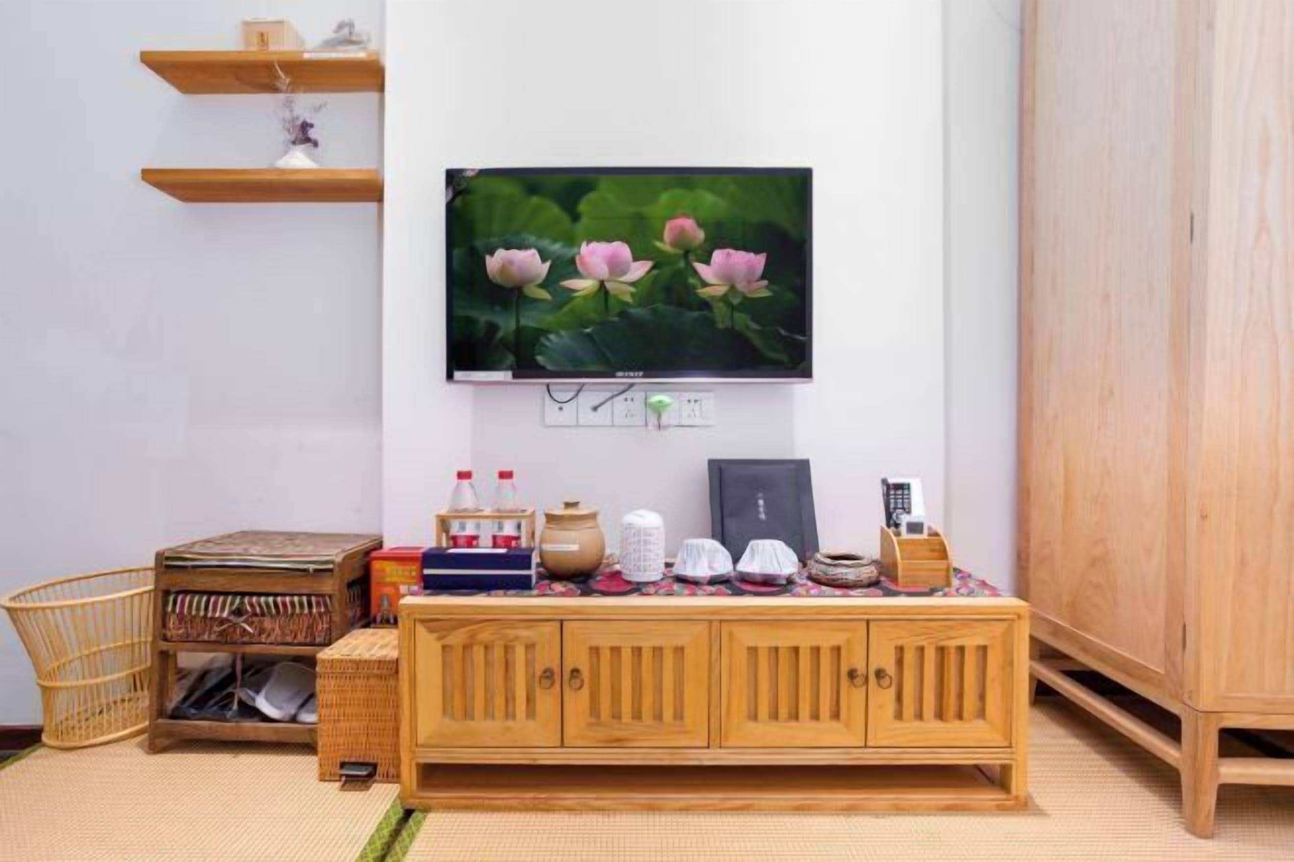 Una sala de estar con un televisor montado en la pared, un mueble de madera, una mesita pequeña y una cesta tejida.