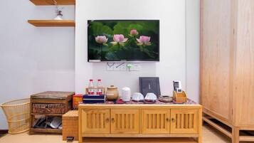 Una sala de estar con un televisor montado en la pared, un mueble de madera, una mesita pequeña y una cesta tejida.