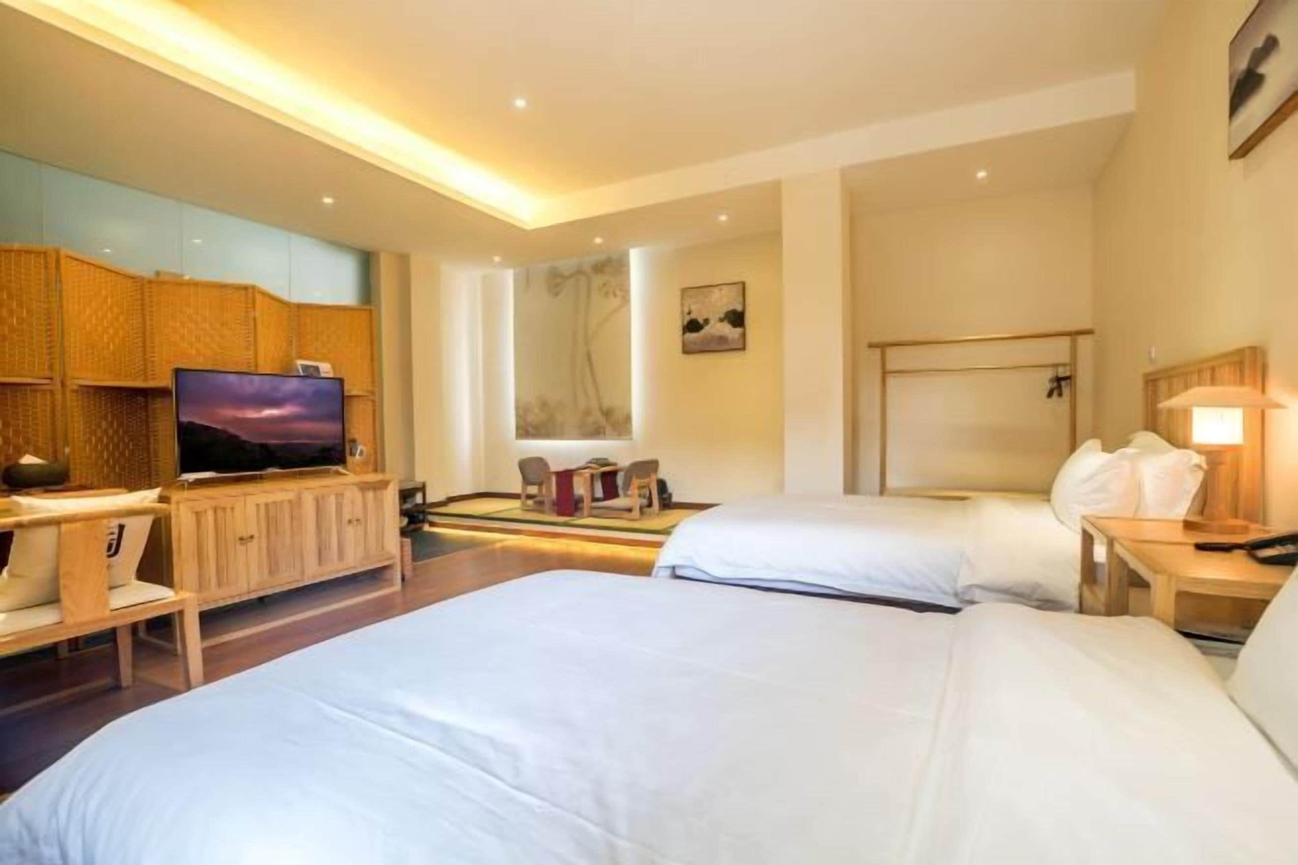 A hotel room with two beds, a television, a desk with a chair, and a wall-mounted TV.