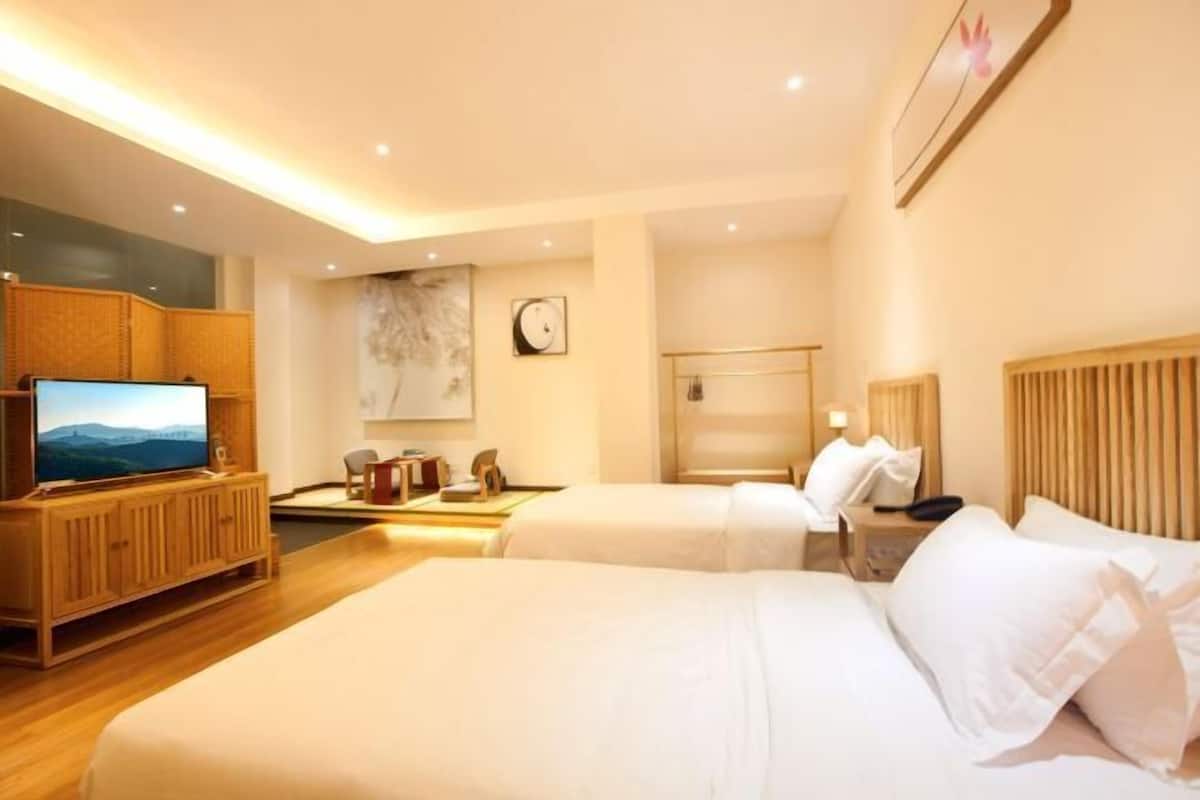 Habitación de hotel con dos camas, un televisor, un mueble de madera y una obra de arte colgada en la pared.