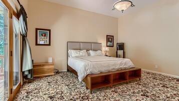 A bedroom with a large bed, a wooden bench, a nightstand, a lamp, and a ceiling light fixture.