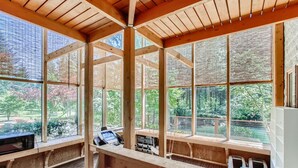 Una habitación amplia con ventanas grandes, vigas de madera y vistas a un jardín.