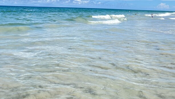 A beach with clear blue water and a partly cloudy sky.