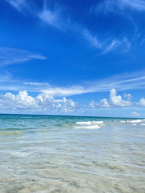 Ein Strand mit klarem, blauem Wasser und einem teilweise bewölkten Himmel.
