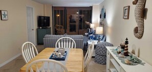 Un comedor con una mesa de madera, sillas y un televisor al fondo.