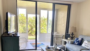 A living room with a television, a sofa, a coffee table, and a sliding glass door leading to a balcony.