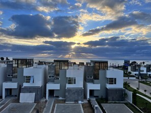 A modern residential complex with multiple buildings, a clear view of the sea, and a sunset in the background.