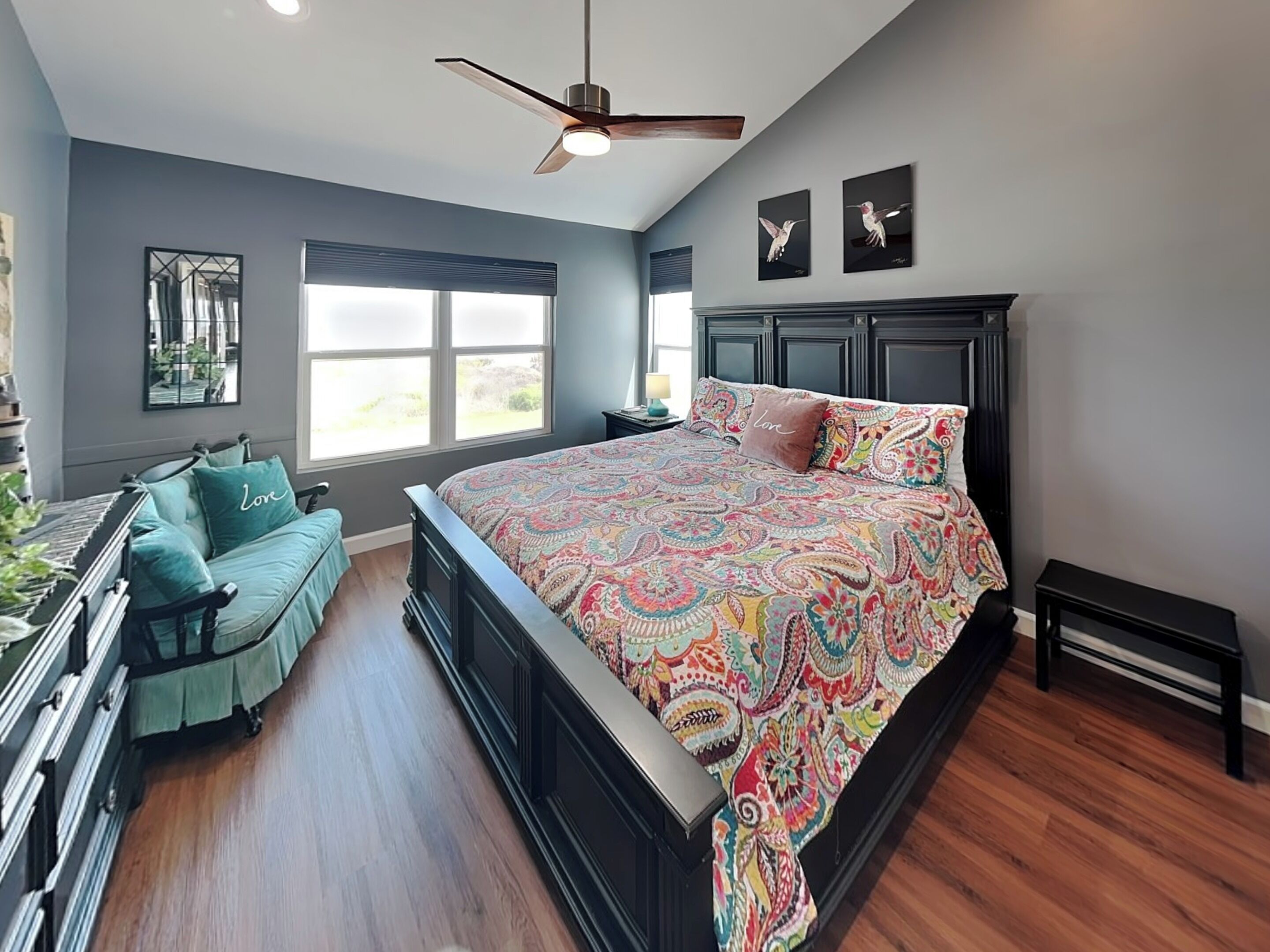 A bedroom with a bed, a desk, a chair, a ceiling fan, and a window.